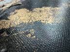 Macro of gold pigment scattered across the dark canvas weave of Unfold