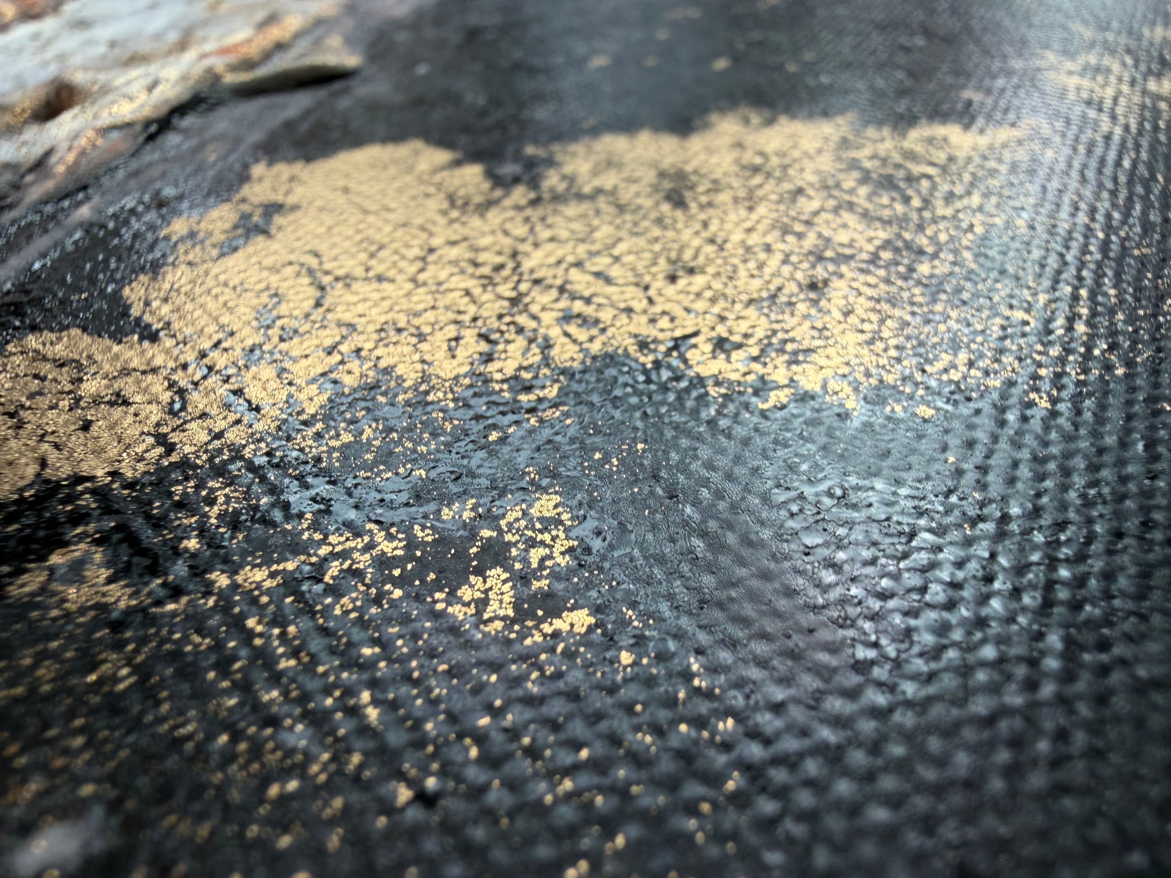 Macro of gold pigment scattered across the dark canvas weave of Unfold